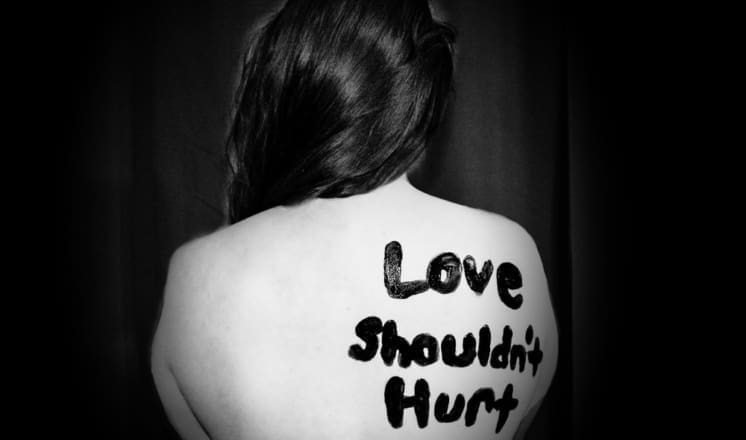 "Love Shouldn't Hurt" written in black on a woman's back.