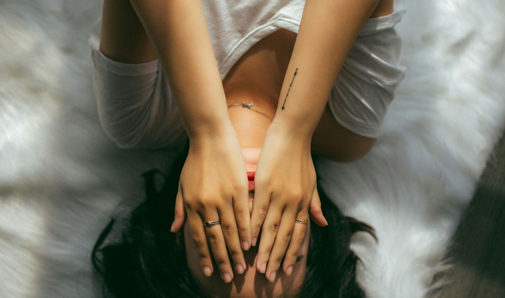 A person lies on their back, covering their face with their hands.